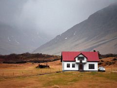 08B A single white house with a red roof with mountains behind on the drive from Borgarnes to Snaefellsnes Iceland